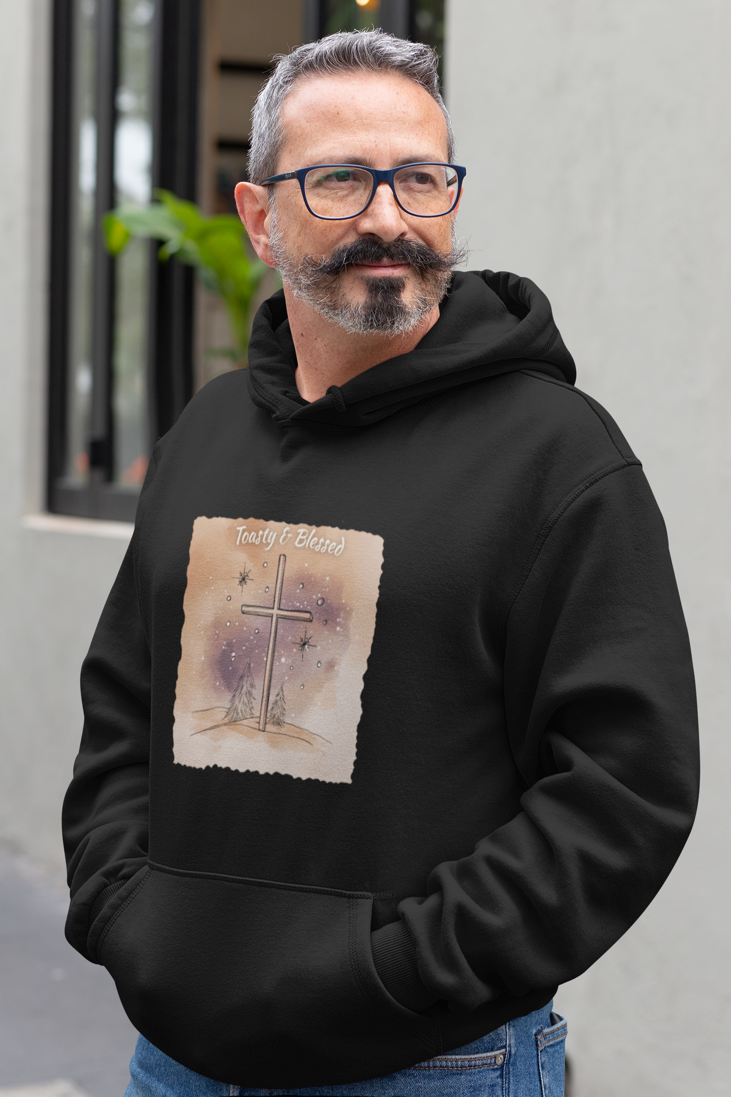 Man wearing a black hoodie with a watercolor graphic cross design on it, standing outdoors.